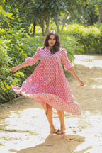 A woman is seen running or dancing in a pinkish floral printed handmade cotton mini dress in an outdoor setting.