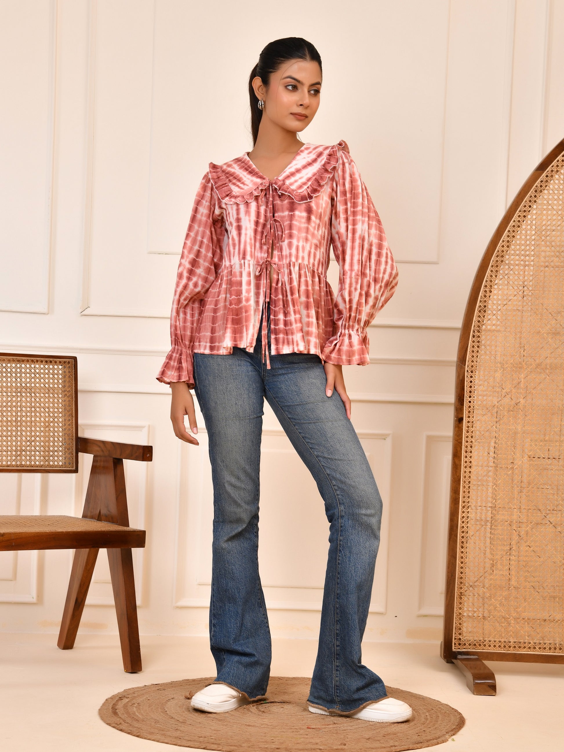 Woman wearing a red plaid shirt and blue jeans standing in a room with wooden furniture.