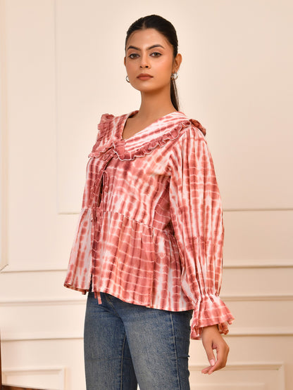 Woman wearing a pink tie-dye blouse with ruffled details against a beige wall.