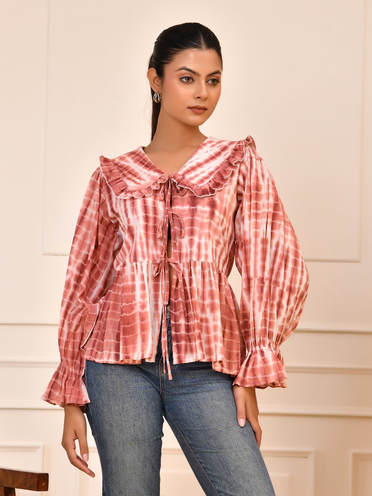 Woman wearing a red and white checkered blouse with blue jeans against a neutral background