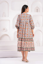 Woman wearing a patterned dress standing against a white abstract wall.