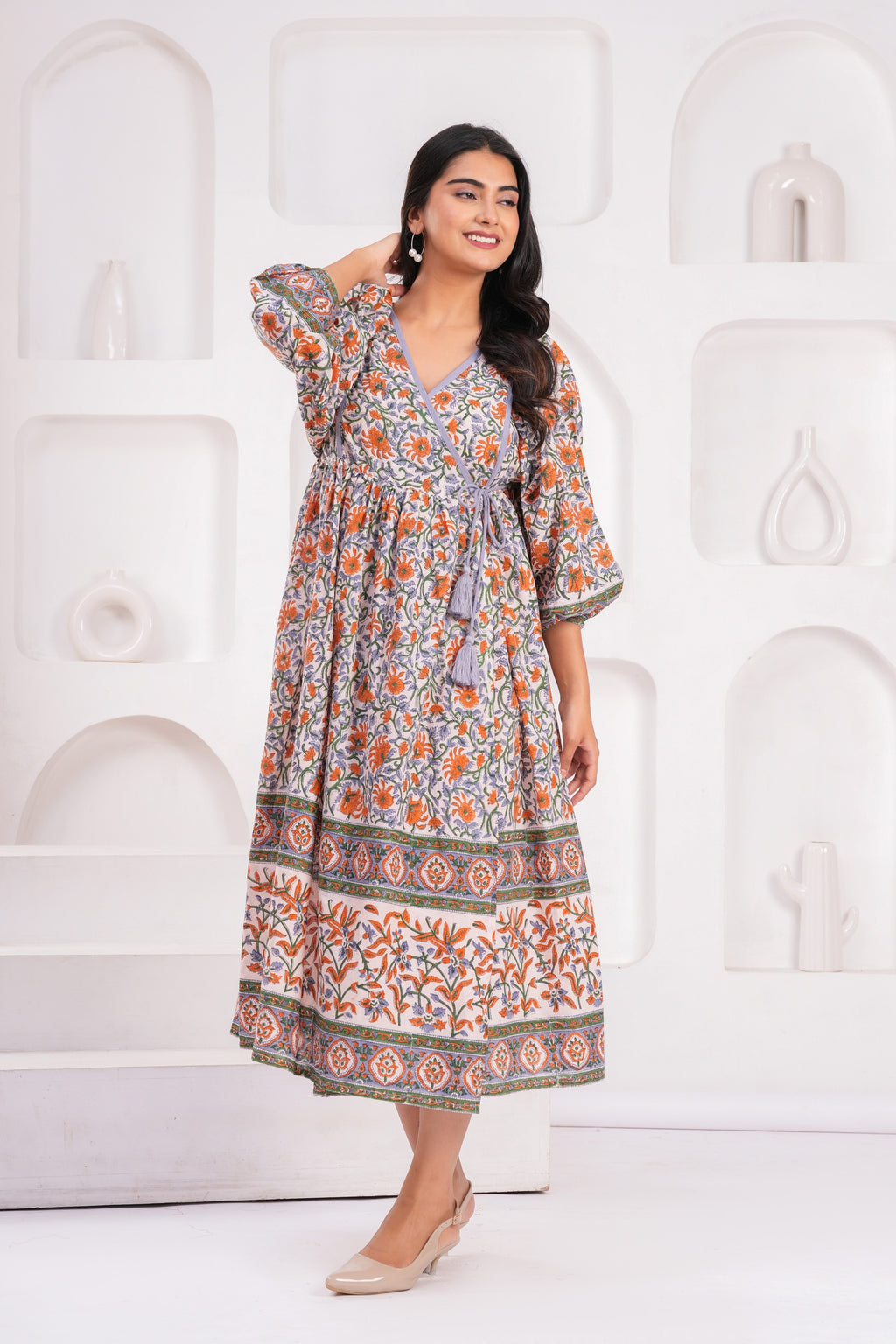 Woman wearing a patterned dress standing against a white decorative wall.