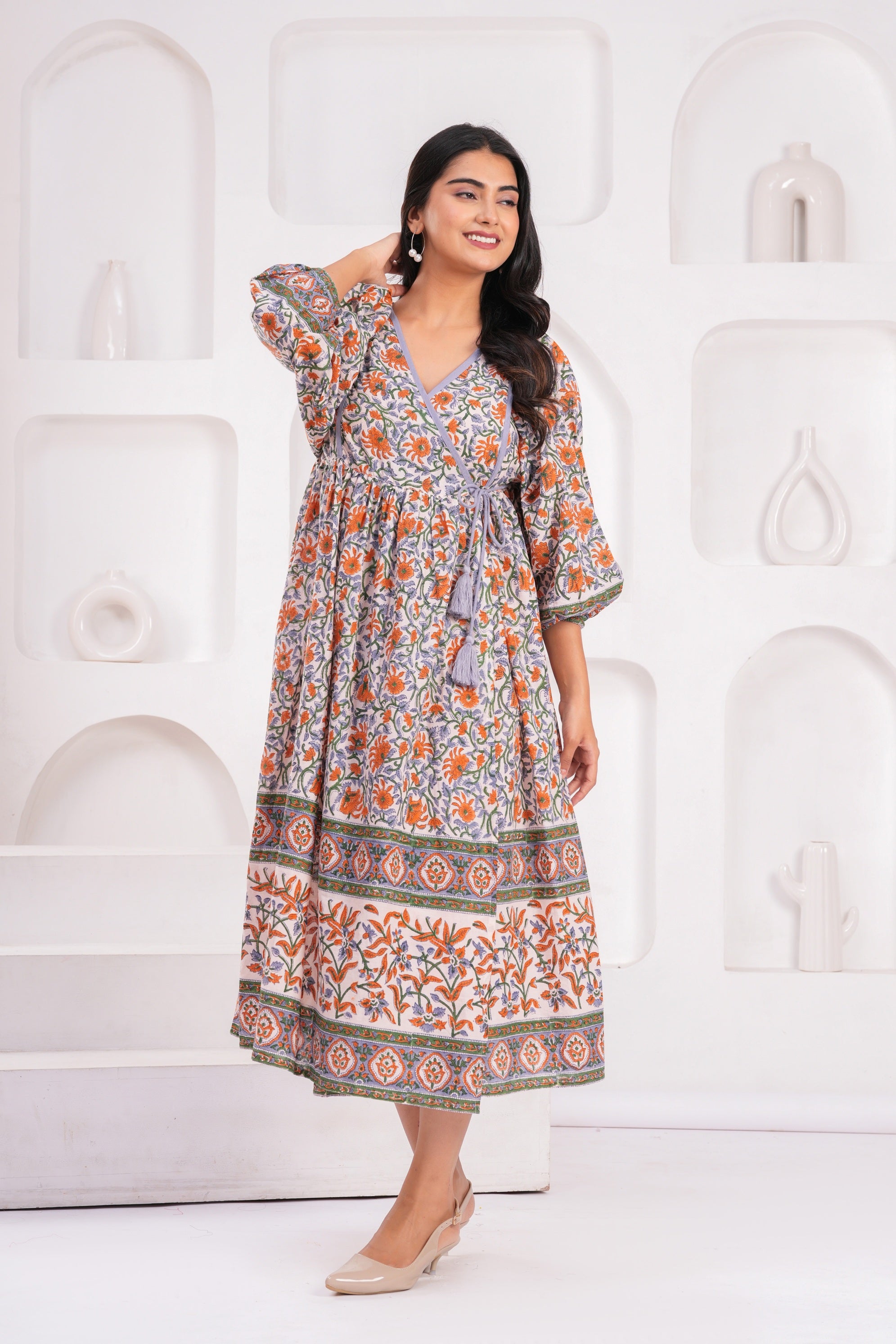 Woman wearing a patterned dress standing against a white decorative wall.