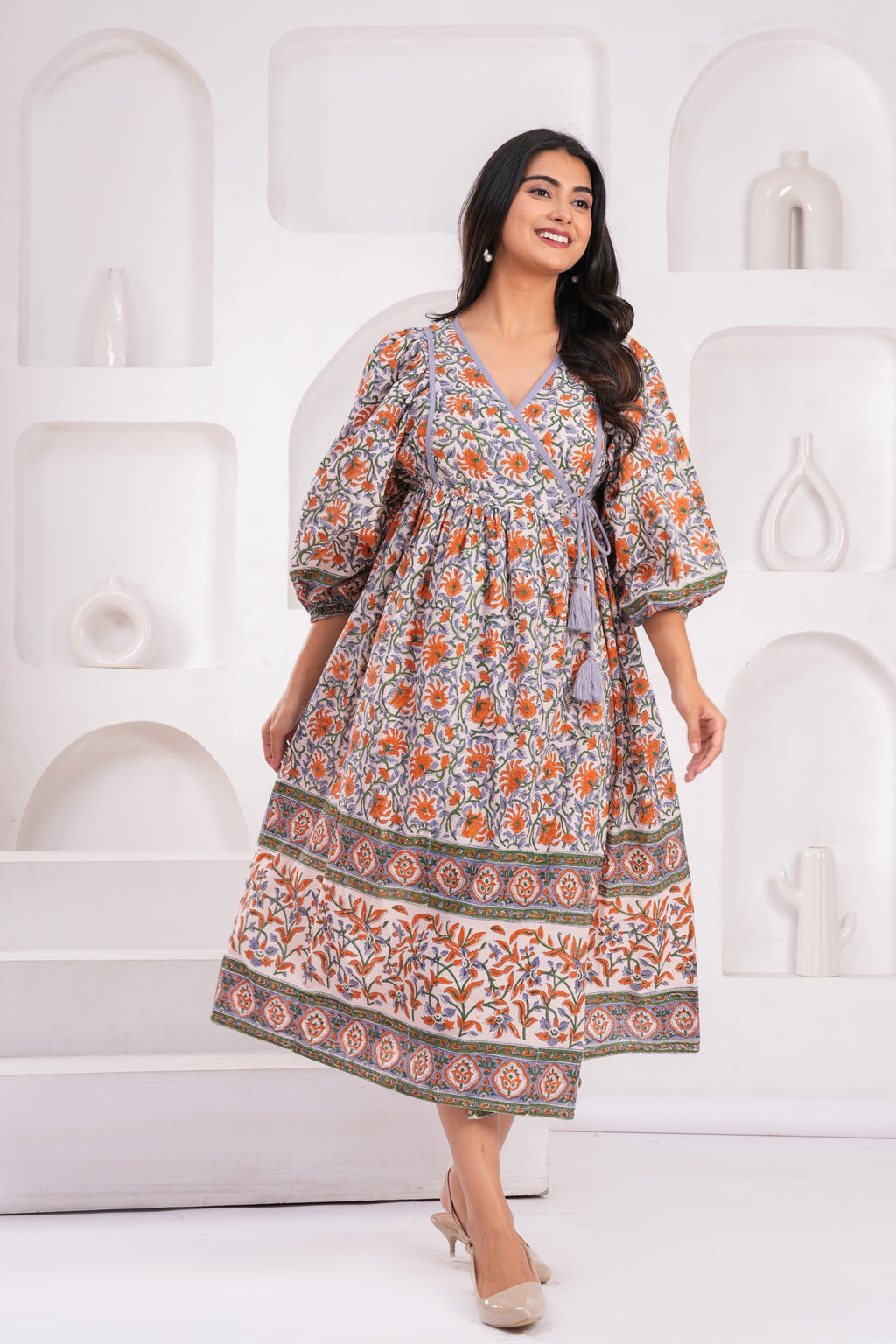Woman wearing a patterned dress against a white decorative wall.
