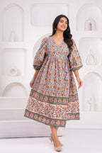 Woman wearing a patterned dress against a white decorative wall.