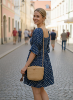 Woman in a blue dress with a straw bag walking down a street.